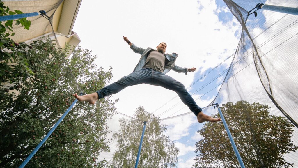 Man performing a midair trampoline jump outdoors beneath a cloudy sky.