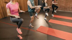 A group performs high knees together in an indoor fitness studio with yoga mats.