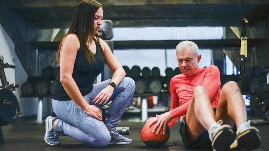 A senior man exercising with a personal trainer in a gym, focusing on core workouts.