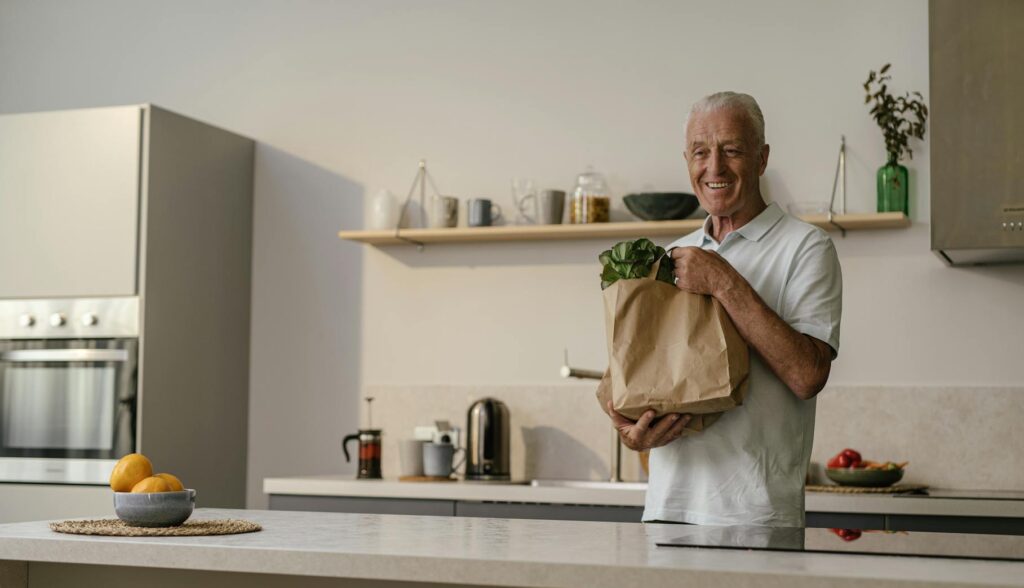 Senior man enjoying a moment in a modern kitchen with fresh groceries.